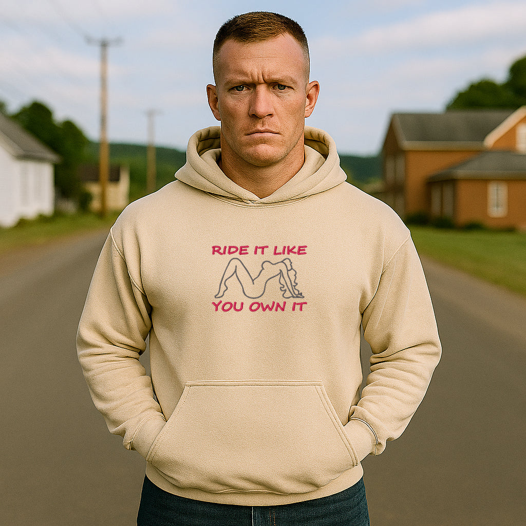 Man wearing a beige hoodie with a graphic and text on a road with houses in the background
